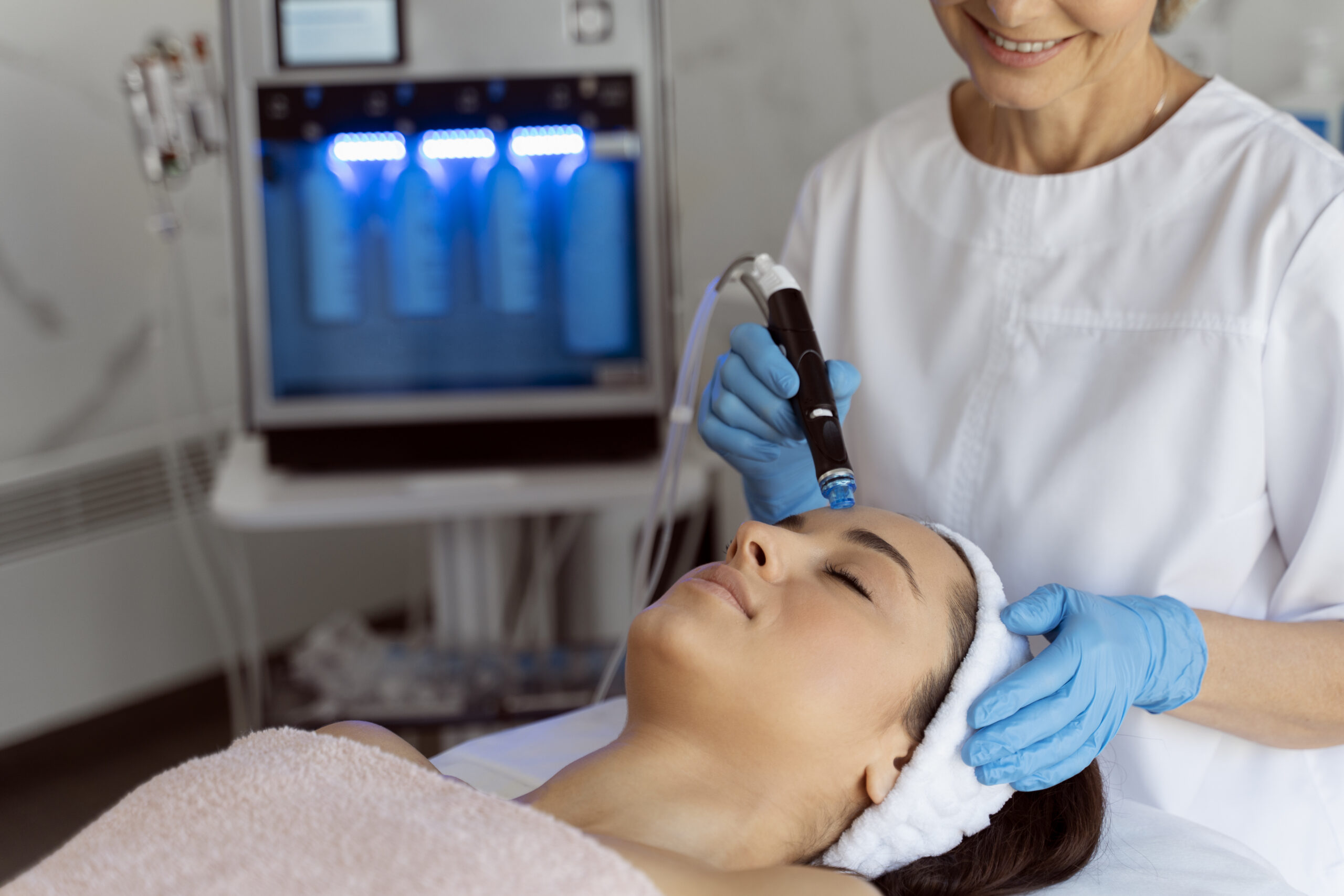 Professional female cosmetologist doing hydra-facial procedure in cosmetology clinic. Doctor using hydra vacuum cleaner. Rejuvenation and cosmetology concept